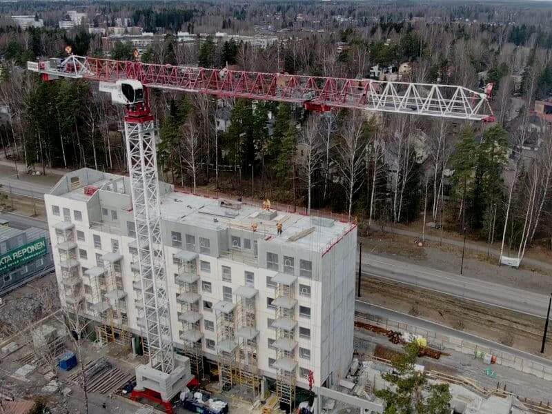 Kerrostalon rakennustyömaa, jossa torninosturi avustaa betonielementtien asennuksessa. Työmaalla näkyy useita asentajia työskentelemässä ylimmissä kerroksissa.
